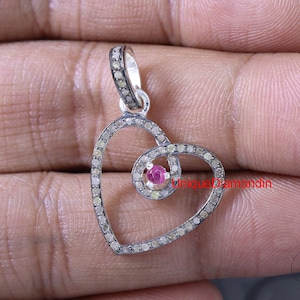 May include: A silver heart-shaped pendant with a smaller heart-shaped swirl in the center. The pendant is set with small diamonds and a single pink gemstone in the center.
