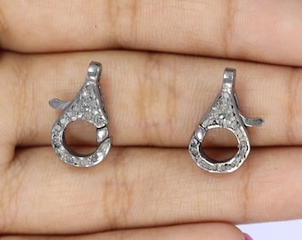 May include: Two silver-toned clasps with a round opening and a small hook. Each clasp is covered in tiny white diamonds.