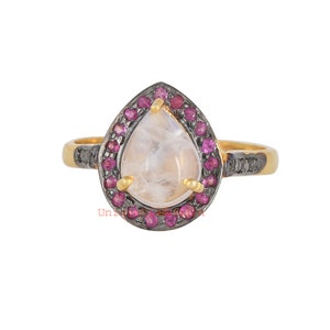 Peut inclure: Une bague en forme de larme nacrée avec un halo de pierres précieuses roses et une bande noire.
