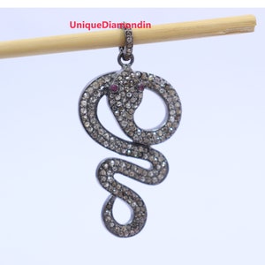 Puede incluir: Un colgante de serpiente de plata con detalles de diamantes negros y rubíes. La serpiente está enroscada y tiene un diseño detallado.