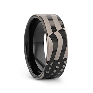 May include: A black and silver tungsten carbide ring with an engraved American flag design.
