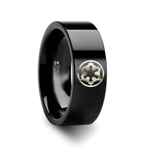 May include: Black tungsten carbide ring with a silver Imperial symbol engraved on the top. The ring is inscribed with "TUNGSTEN CARBIDE".