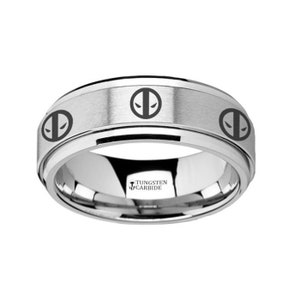 May include: A silver tungsten carbide ring with a black Deadpool logo engraved on the band. The ring has a brushed finish and the words "Tungsten Carbide" are engraved on the inside of the band.