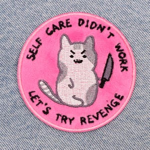Puede incluir: Parche bordado rosa con un gato blanco sosteniendo un cuchillo. El texto alrededor del gato dice "Self care didn't work let's try revenge."