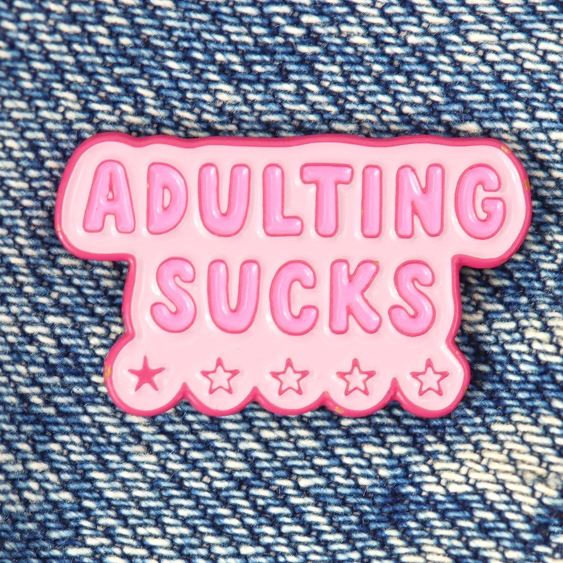 a pink pin with the words adulting sucks on it
