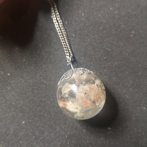 May include: A silver chain necklace with a clear glass orb pendant containing small pieces of colorful material.