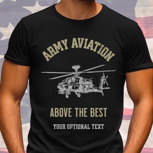 May include: A black short-sleeved t-shirt featuring a graphic of a military helicopter in the center. Above the helicopter is the text ARMY AVIATION in a tan font, and below it is the text ABOVE THE BEST, followed by YOUR OPTIONAL TEXT.