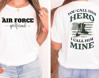 Könnte beinhalten: Weißes T-Shirt mit dem Text "AIR FORCE girlfriend" auf der Vorderseite und "YOU CALL HIM HERO I CALL HIM MINE" mit einer Grafik von Militärstiefeln und einer amerikanischen Flagge auf der Rückseite.