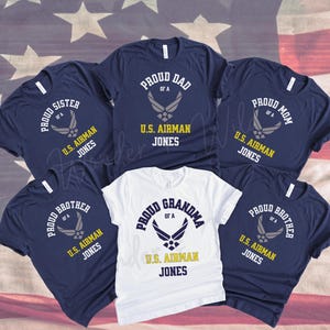 May include: Navy blue and white t-shirts with text and a graphic. The shirts say "Proud Dad", "Proud Mom", "Proud Sister", "Proud Brother", and "Proud Grandma" with "U.S. Airman Jones" below. The shirts have a U.S. Air Force emblem.