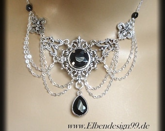 May include: A silver necklace with a large black gemstone pendant and multiple chains. The pendant is surrounded by intricate floral designs. The necklace is on a mannequin's neck.