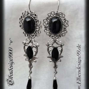 May include: A pair of silver earrings with black gemstone accents. The earrings feature a delicate filigree design and dangle from a hook.