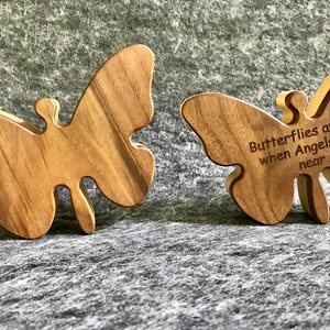 Może przedstawiać: Dwa drewniane ozdoby w kształcie motyla. Jeden motyl jest gładki, drugi ma wygrawerowany tekst "Butterflies appear when Angels are near".