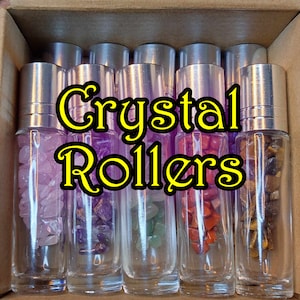 May include: A set of six clear glass roller bottles filled with various coloured crystals. The bottles have silver caps and are labelled "Crystal Rollers".