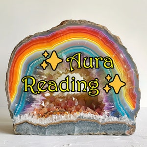 May include: A colorful agate geode with a rainbow pattern and a crystal cave inside. The geode is a natural stone and has a rough, textured surface. The text "Aura Reading" is written in yellow letters on the geode.