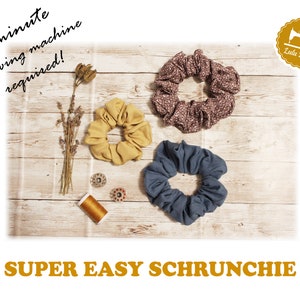 K&ouml;nnte beinhalten: Drei Stoff-Haargummis in verschiedenen Farben und Mustern auf einer Holzoberfl&auml;che. Die Haargummis sind gelb, braun und blau. Der Text "SUPER EASY SCHRUNCHIE" befindet sich am unteren Rand des Bildes. Der Text "15 Minuten, keine N&auml;hmaschine erforderlich!" befindet sich am oberen Rand des Bildes. Ein N&auml;hmaschinen-Symbol mit dem Text "Lulu Baby" befindet sich in der oberen rechten Ecke des Bildes.