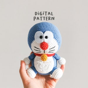 May include: Crochet amigurumi pattern for a blue and white cat with a red nose and yellow collar. The pattern is called "Digital Pattern".