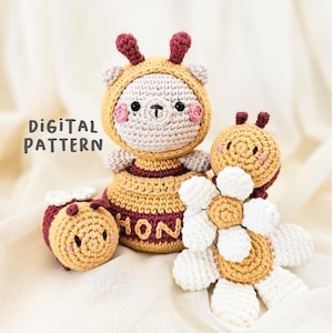 May include: A collection of handmade crochet toys, including a bear in a bee costume, a bee, and a flower. The bear wears a yellow and maroon striped outfit with the word "HON" on it. The text "DIGITAL PATTERN" is visible.