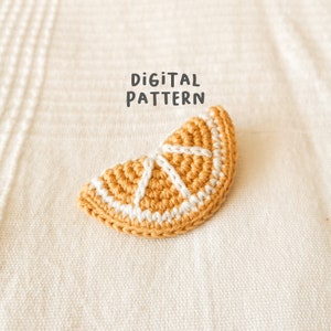 May include: A crocheted orange slice with white stitching, laying on a white textured surface. The text "DIGITAL PATTERN" is written above the orange slice.