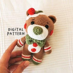May include: A crocheted gingerbread bear toy with red and white accents. The bear is wearing a green bow tie and has a brown, white, and green face.