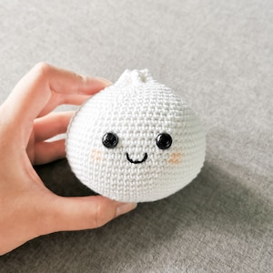 May include: A white crocheted dumpling with a smiling face, black eyes, and pink cheeks.