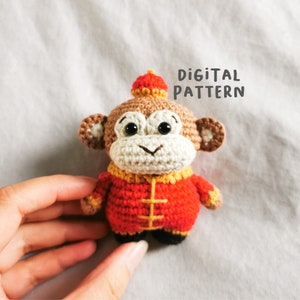 Może przedstawiać: Pluszowa zabawka amigurumi małpy wykonana na szydełku w tradycyjnym chińskim stroju w kolorze czerwonym i żółtym. Małpa ma brązowe futro, czarne oczy i białą twarz. Zabawka trzyma czerwony i żółty kapelusz.