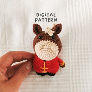 May include: Crochet pattern for a brown and beige horse wearing a red and yellow Chinese-style outfit. The pattern is called "Digital Pattern".