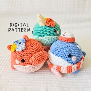 May include: Three handmade crochet whale plushies in coral, teal, and blue. Each whale has a unique design, including a flower crown, a unicorn horn, and a winter hat with a scarf. The text "Digital Pattern" is visible.