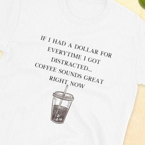 May include: White t-shirt with a black and white illustration of a cup of iced coffee and the text "IF I HAD A DOLLAR FOR EVERYTIME I GOT DISTRACTED... COFFEE SOUNDS GREAT RIGHT NOW".