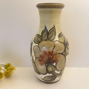 May include: A ceramic vase with a cream background and a floral design in shades of brown, beige, and red. The vase has a rounded body and a narrow neck.