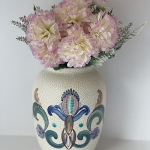 Könnte beinhalten: Eine weiße Keramikvase mit craquelé-Glasur und einem floralen Design in Blau, Grün und Rosa. Die Vase ist mit einem Strauß rosa und weißer Nelken gefüllt.