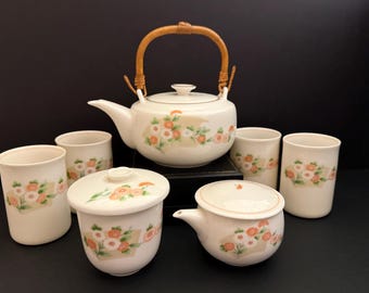May include: A white porcelain teapot with a floral design and a bamboo handle, along with six matching cups and two lids.