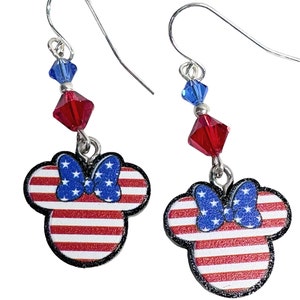 May include: A pair of silver dangle earrings featuring a red, white, and blue American flag design with a blue bow. The earrings are accented with red and blue crystal beads.