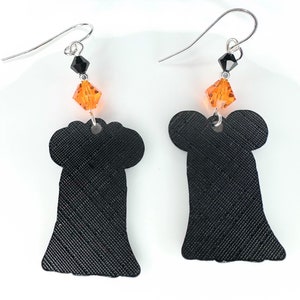 Puede incluir: Un par de pendientes de fantasma negro con acentos de cristal naranja. Los pendientes est&aacute;n hechos de un material texturizado y tienen un dise&ntilde;o colgante.
