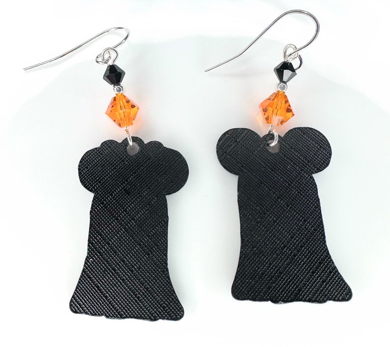 Puede incluir: Un par de pendientes de fantasma negro con acentos de cristal naranja. Los pendientes est&aacute;n hechos de un material texturizado y tienen un dise&ntilde;o colgante.