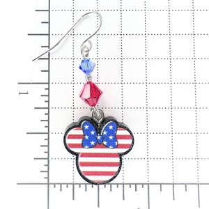 May include: Red, white, and blue American flag themed Minnie Mouse earrings with crystal accents. The earrings are made of wood and have a silver hook.