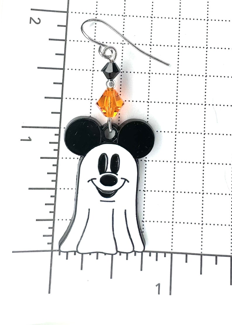 Puede incluir: Fantasma blanco y negro con orejas de Mickey Mouse y una cara sonriente. El fantasma lleva una cuenta negra y una cuenta de cristal naranja.
