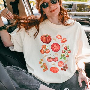 Könnte beinhalten: Ein weißes T-Shirt mit einer Aquarell-Illustration von roten Tomaten, darunter ganze Tomaten, Tomatenscheiben und Kirschtomaten.