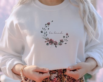 May include: White sweatshirt featuring a floral wreath design with the text "be kind" in the centre.