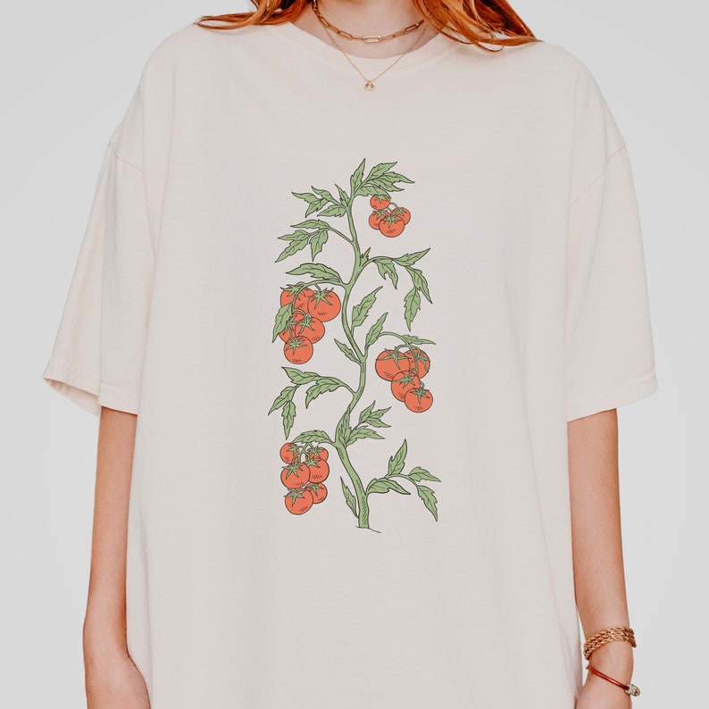 May include: A white t-shirt with a graphic of a tomato plant with red tomatoes on it.