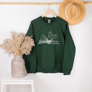 May include: A dark green sweatshirt with a white graphic of an open book and the text "the book was better".