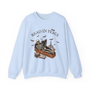 May include: Light blue sweatshirt with a skeleton reading a book in a coffin. The text "READ IN PEACE" is printed on the front of the sweatshirt.