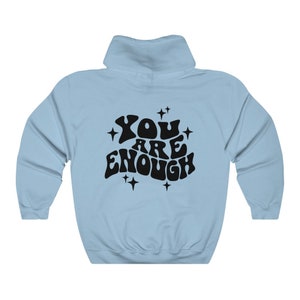 Puede incluir: Sudadera con capucha azul claro con un estampado gr&aacute;fico negro que dice "YOU ARE ENOUGH" en una fuente retro con estrellas alrededor del texto.