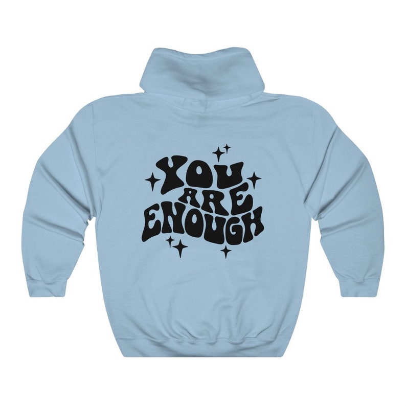 Puede incluir: Sudadera con capucha azul claro con un estampado gr&aacute;fico negro que dice "YOU ARE ENOUGH" en una fuente retro con estrellas alrededor del texto.