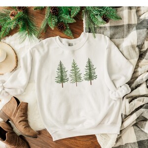 May include: White sweatshirt with a graphic of three green pine trees.