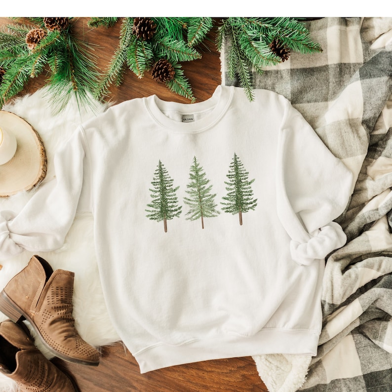 May include: White sweatshirt with a graphic of three green pine trees.