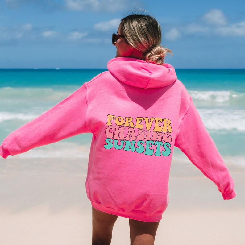May include: Pink hoodie with the text "FOREVER CHASING SUNSETS" in a retro font on the back.