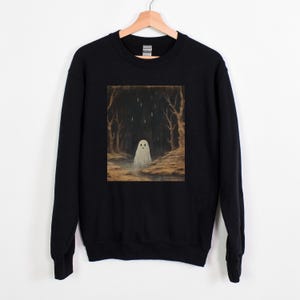 Puede incluir: Sudadera negra con un estampado gr&aacute;fico de un fantasma blanco en un bosque oscuro. El fantasma tiene una peque&ntilde;a cara amigable.