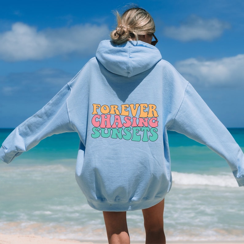May include: A light blue hoodie with the text "FOREVER CHASING SUNSETS" in a retro font with pink, orange, and green colors.