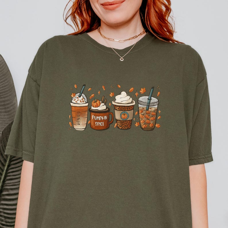 May include: A green t-shirt with a graphic of four fall-themed coffee drinks. The drinks are decorated with fall leaves and pumpkins. The text "Pumpkin Spice" is printed on the shirt.