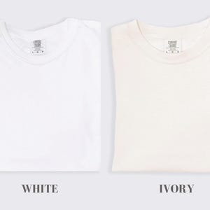 May include: Two plain t-shirts, one white and one ivory, both with a small tag that reads "Comfort Colors" and "L/G".
